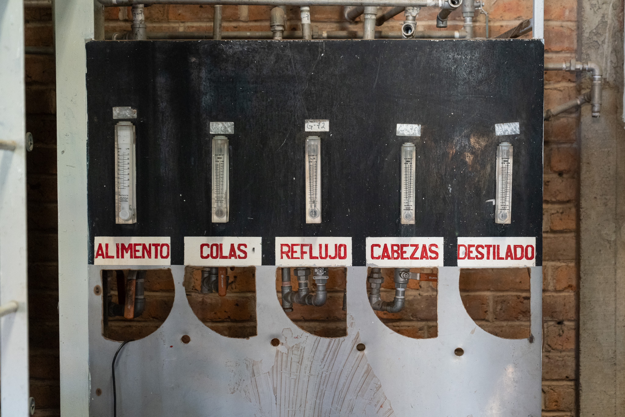 Hand-painted flow gauges on a distillery still panel labelled alimento, colas, reflujo, cabezas, destilado.