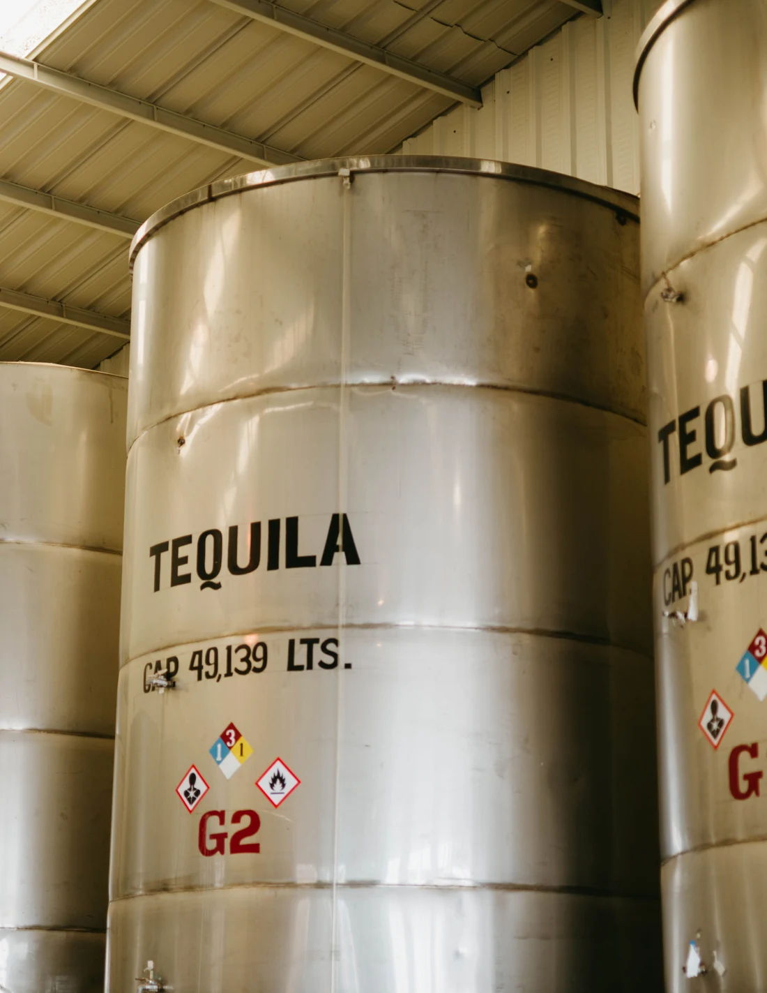 Rows of tall stainless-steel tanks stencilled TEQUILA inside a Mexican distillery, lit from skylights overhead.