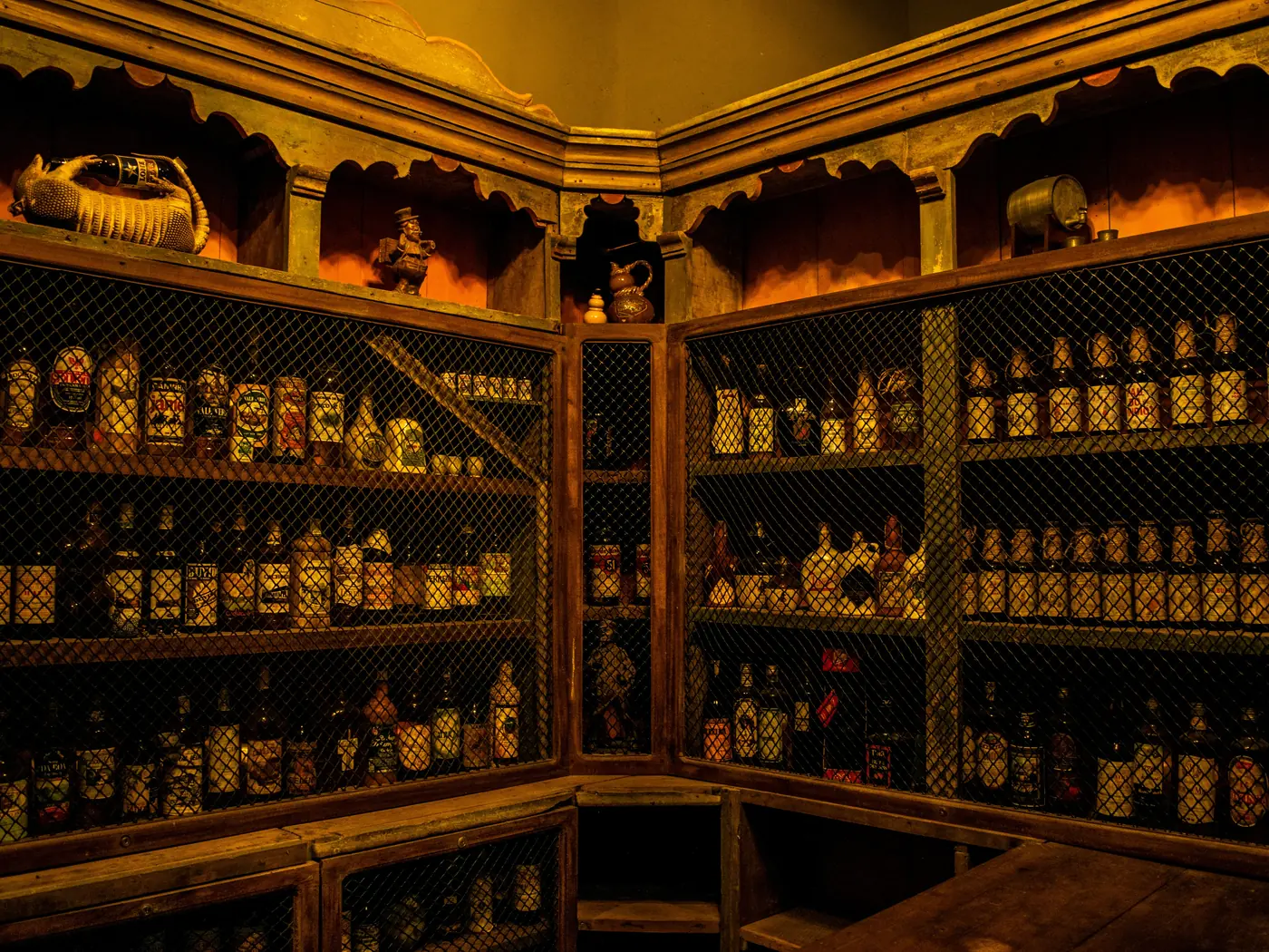 A boutique liquor store cellar, bottles ranked behind wire-fronted wooden shelves under warm low light.